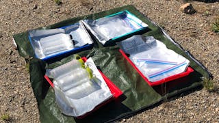 An experimental setup with Nalgene bottles, plastic water bottles, and a plastic bag placed on a reflective tarp exposed to the sunlight during a lower-altitude trial.